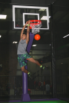 Boy Hanging from Rim of Trampolie Basketball Hoop after Dunking